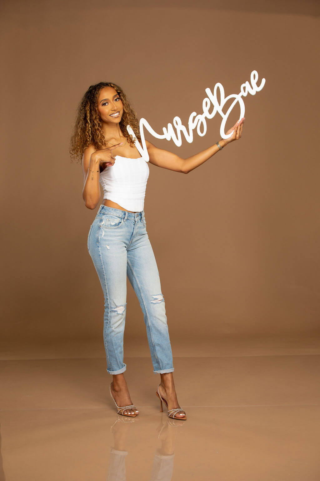 Senior Model is holding a white 36 inch photo prop that says "NurseBae!"