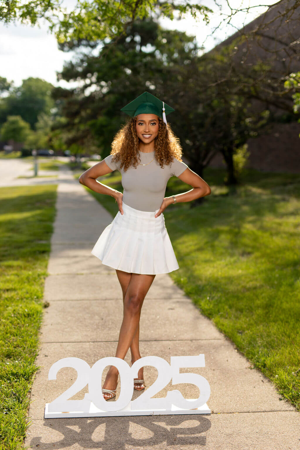 Senior Model standing on a sidewalk  behind giant "2025" photo prop!
