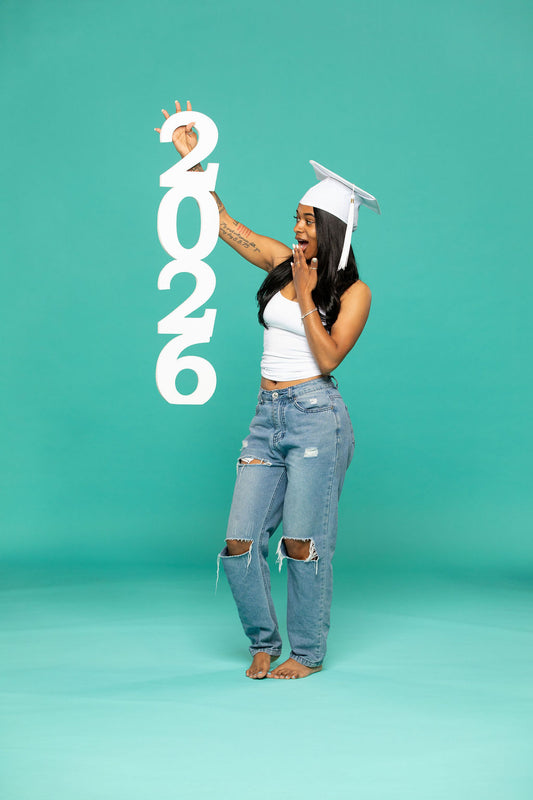 Playful graduate in white cap holding a vertical “2026” prop with a surprised expression. 2026 senior props available now at collageandwood.com.