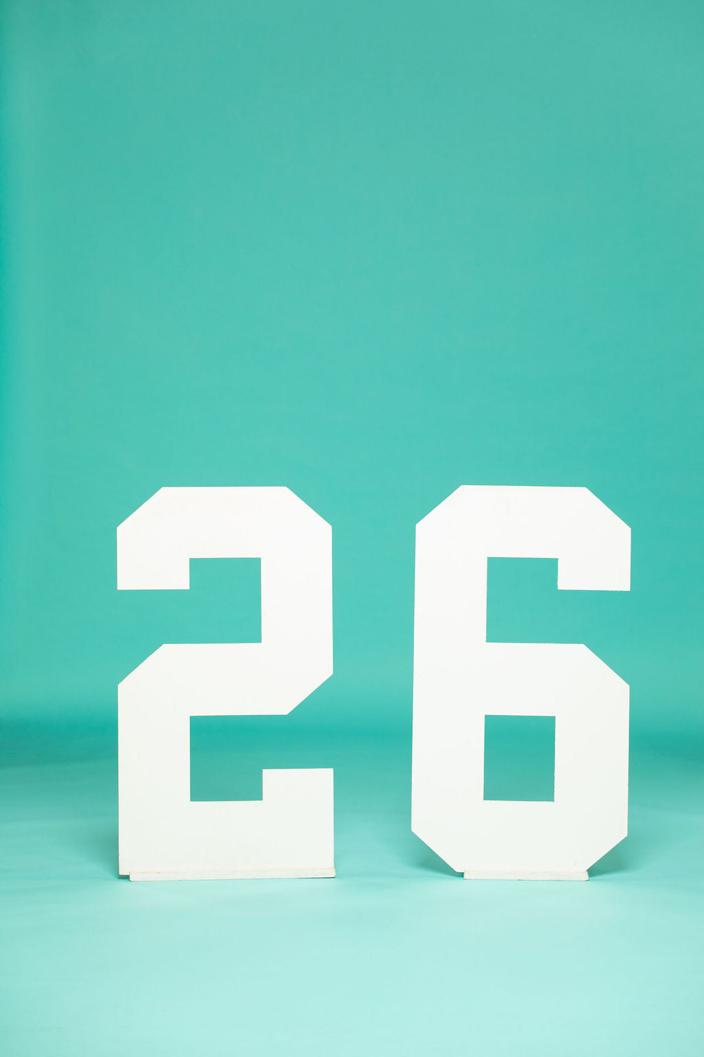 Large white wooden “2” and “6” standing side-by-side on a teal backdrop—ideal for 2026 senior portraits. Available now at collageandwood.com.