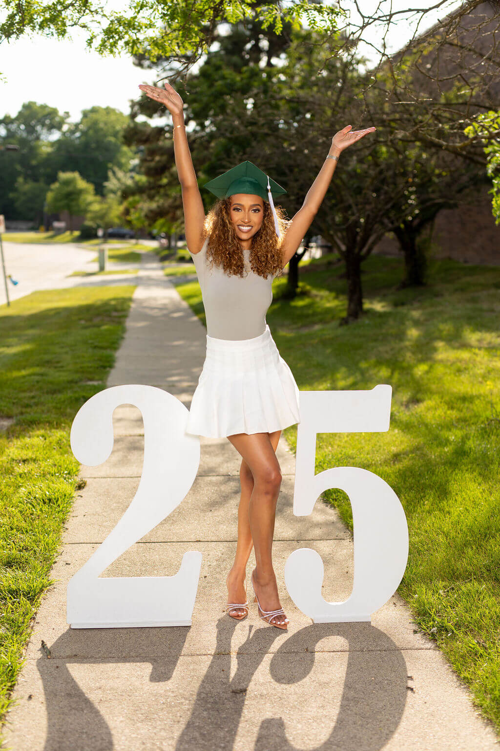 graduation model with arms raised above her head standing between two giant white numbers: 25.