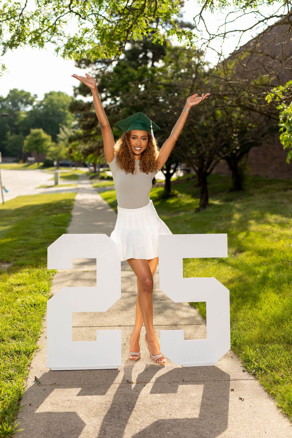 model, arms raised above her head, with graduation cap standing between two giant white numbers: 25.