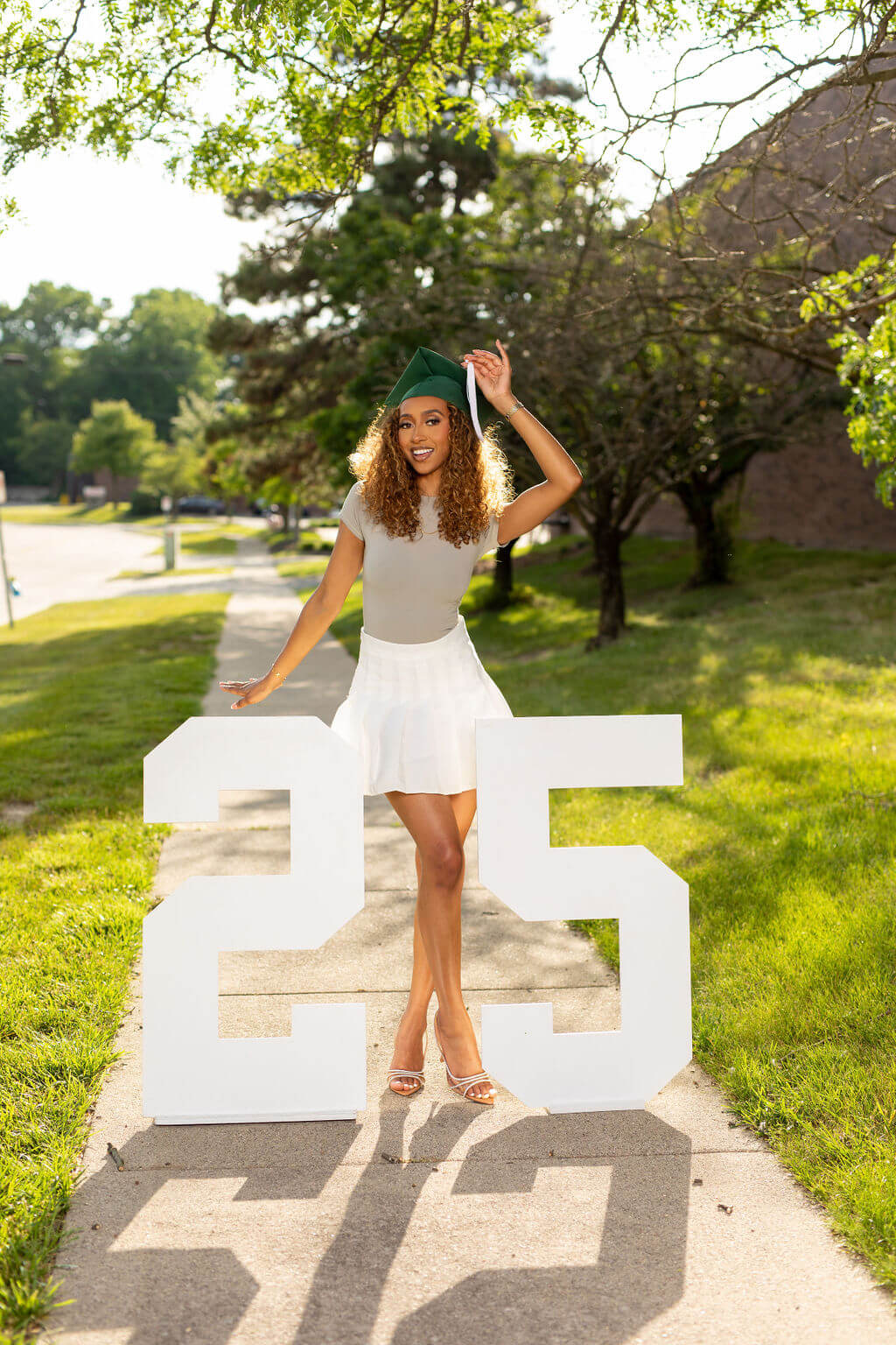 model with graduation cap standing between two giant white numbers: 25.