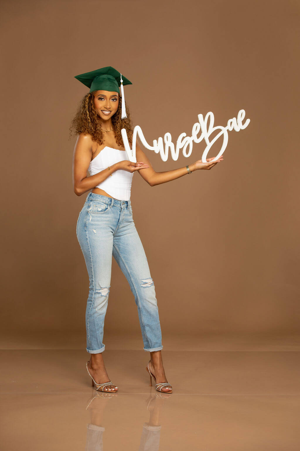 Smiling female model holding "Nurse Bae" photo prop in a professional studio.