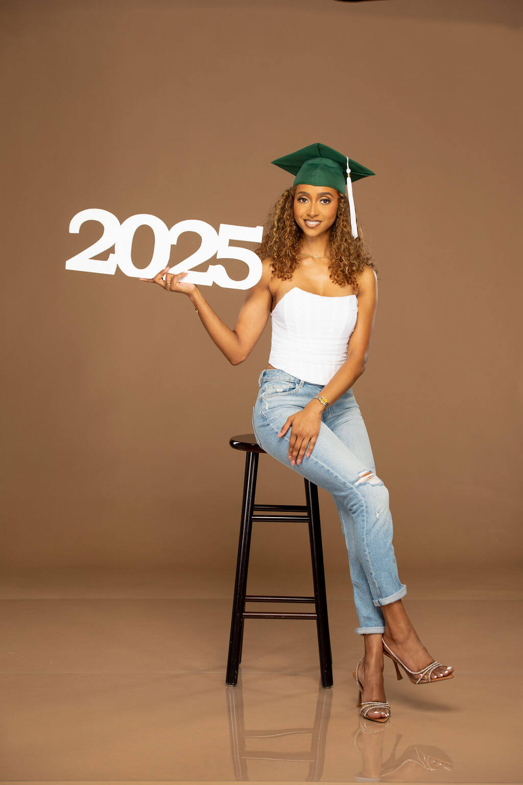 2025 photo prop, held by senior model sitting on stool.