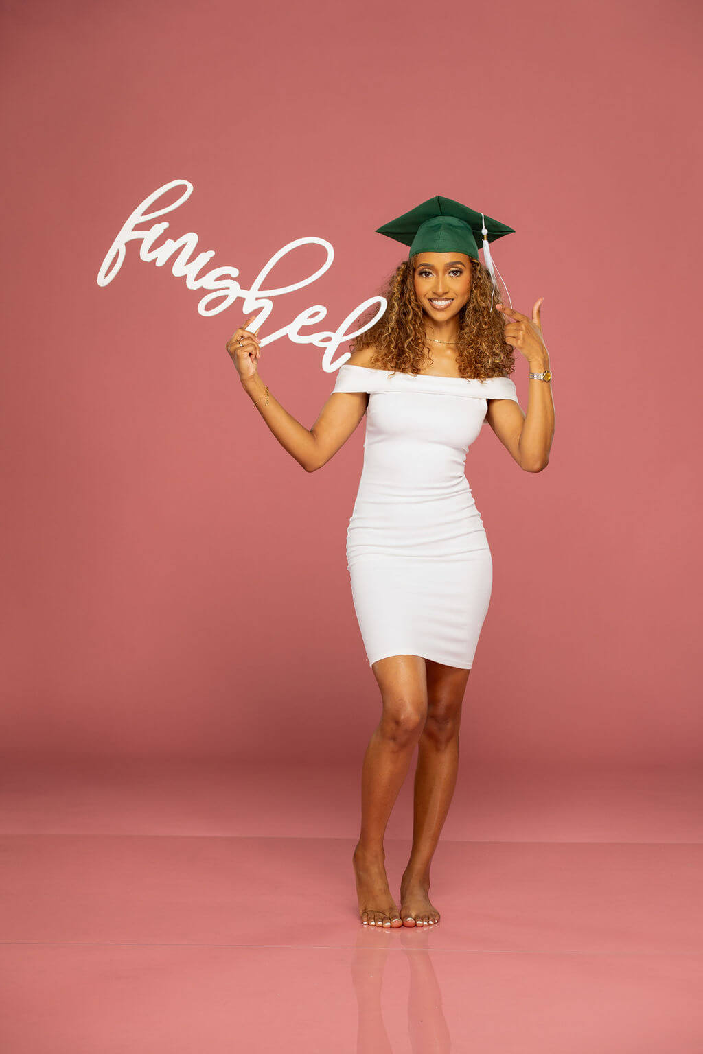 Beautiful senior model with green grad cap holding "Finished" photo prop.