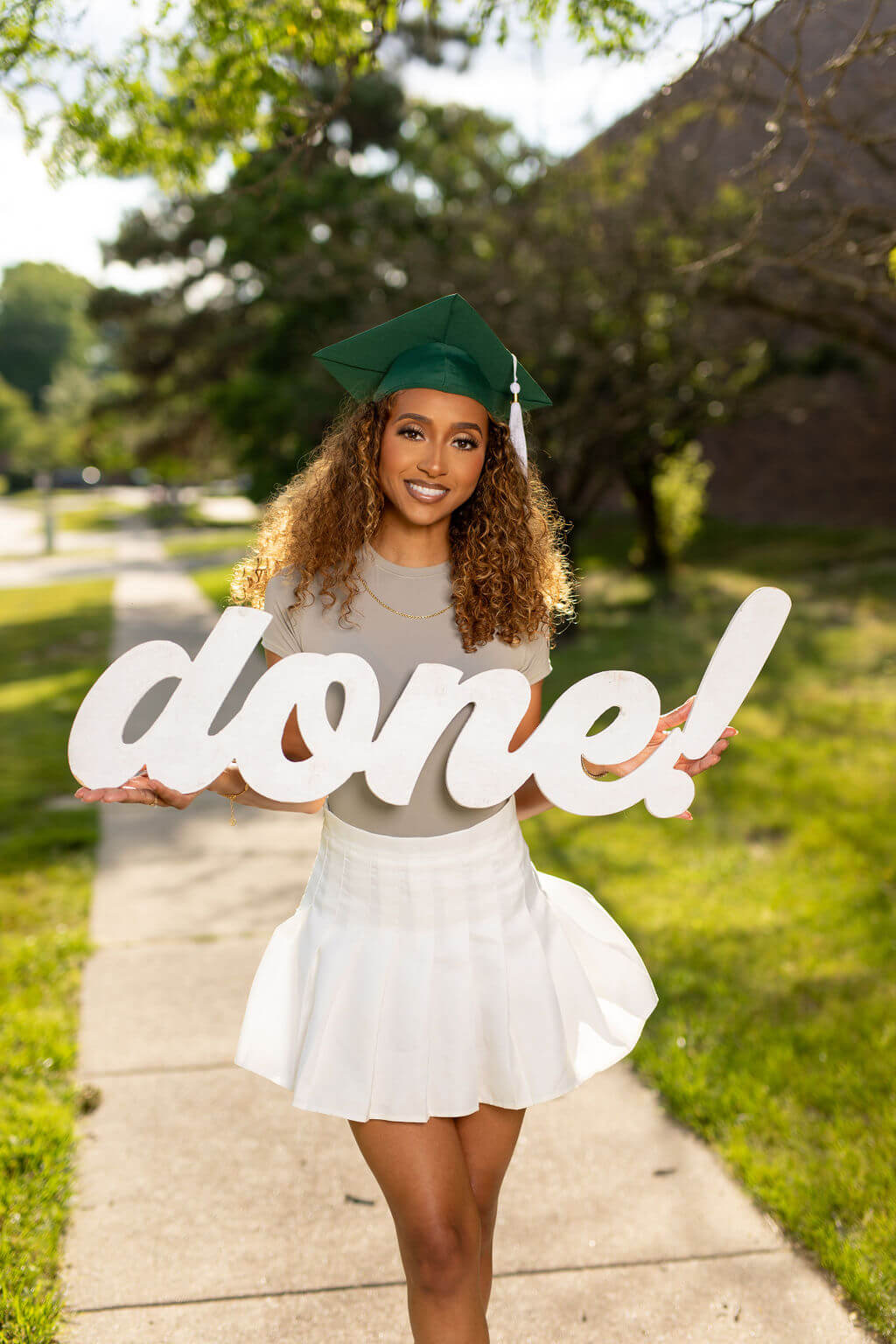 Senior model posing with "done!" photo prop. Model is outside on the sidewalk.