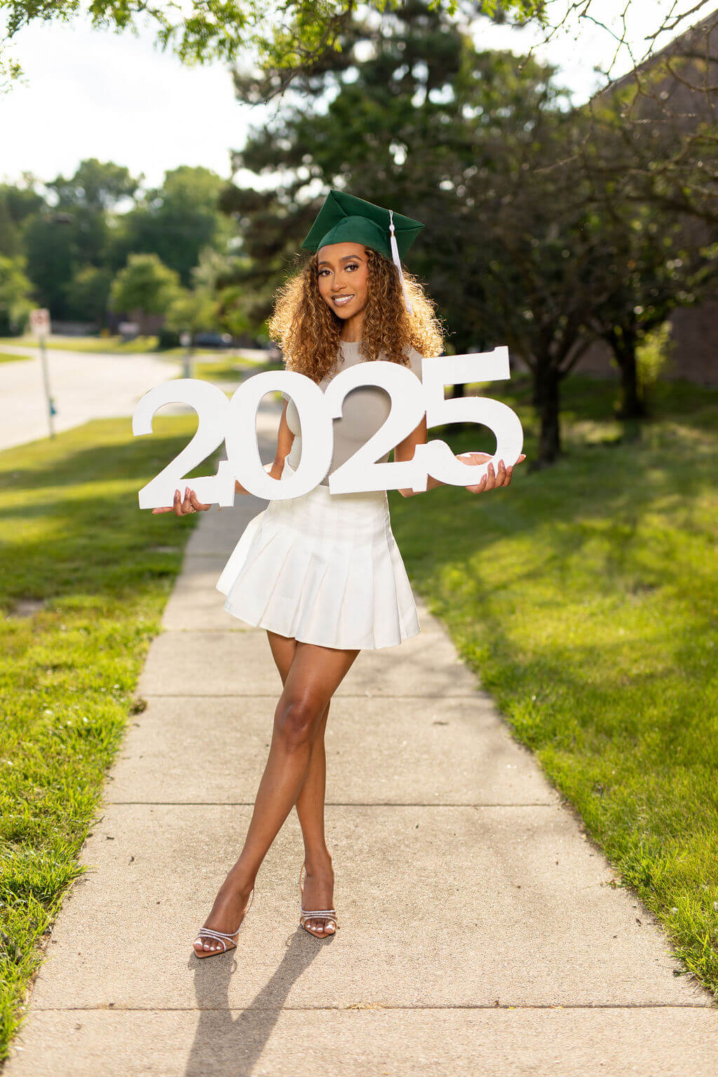 Senior Model holding giant "2025" photo prop while standing on a sidewalk.