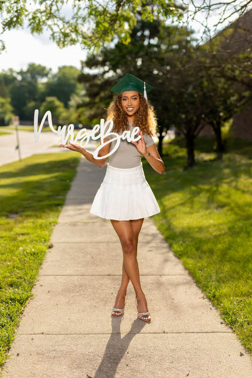 Smiling female model holding "Nurse Bae" photo prop.