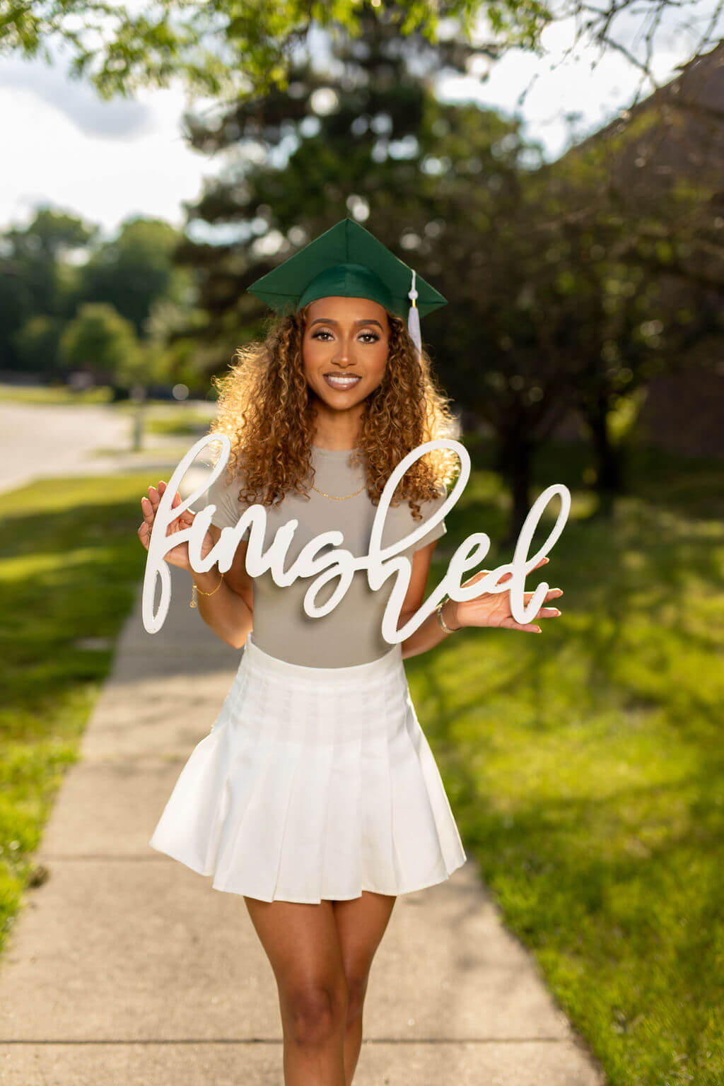 Beautiful senior model with green grad cap holding "Finished" photo prop.