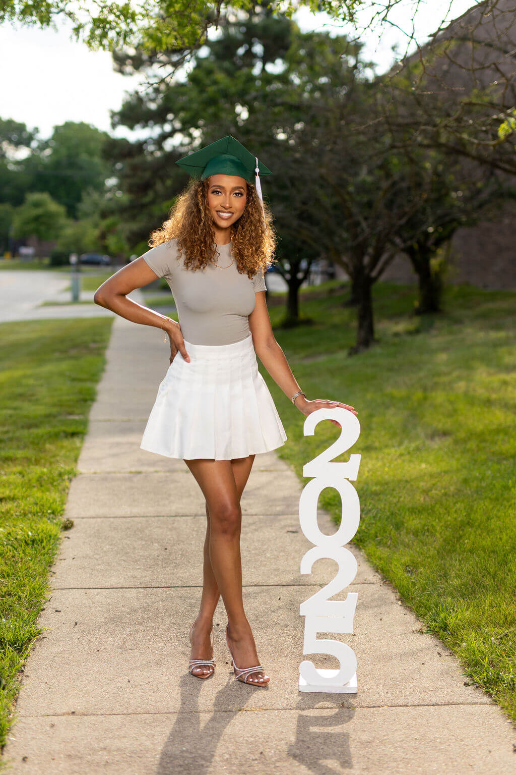 senior model in green graduation cap standing next to 2025 photo vertical prop.