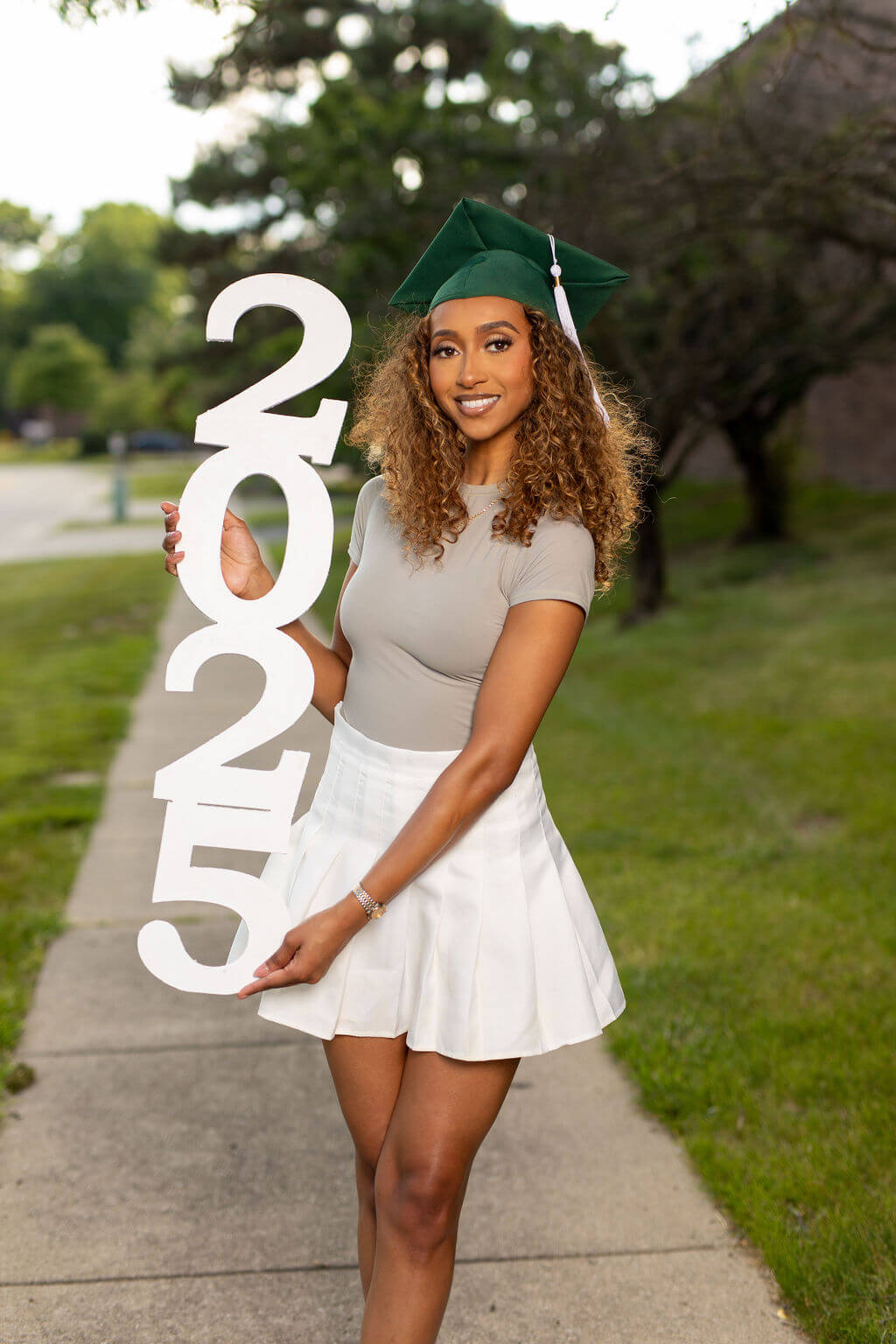 senior model in green graduation cap standing holding 2025 photo vertical prop.