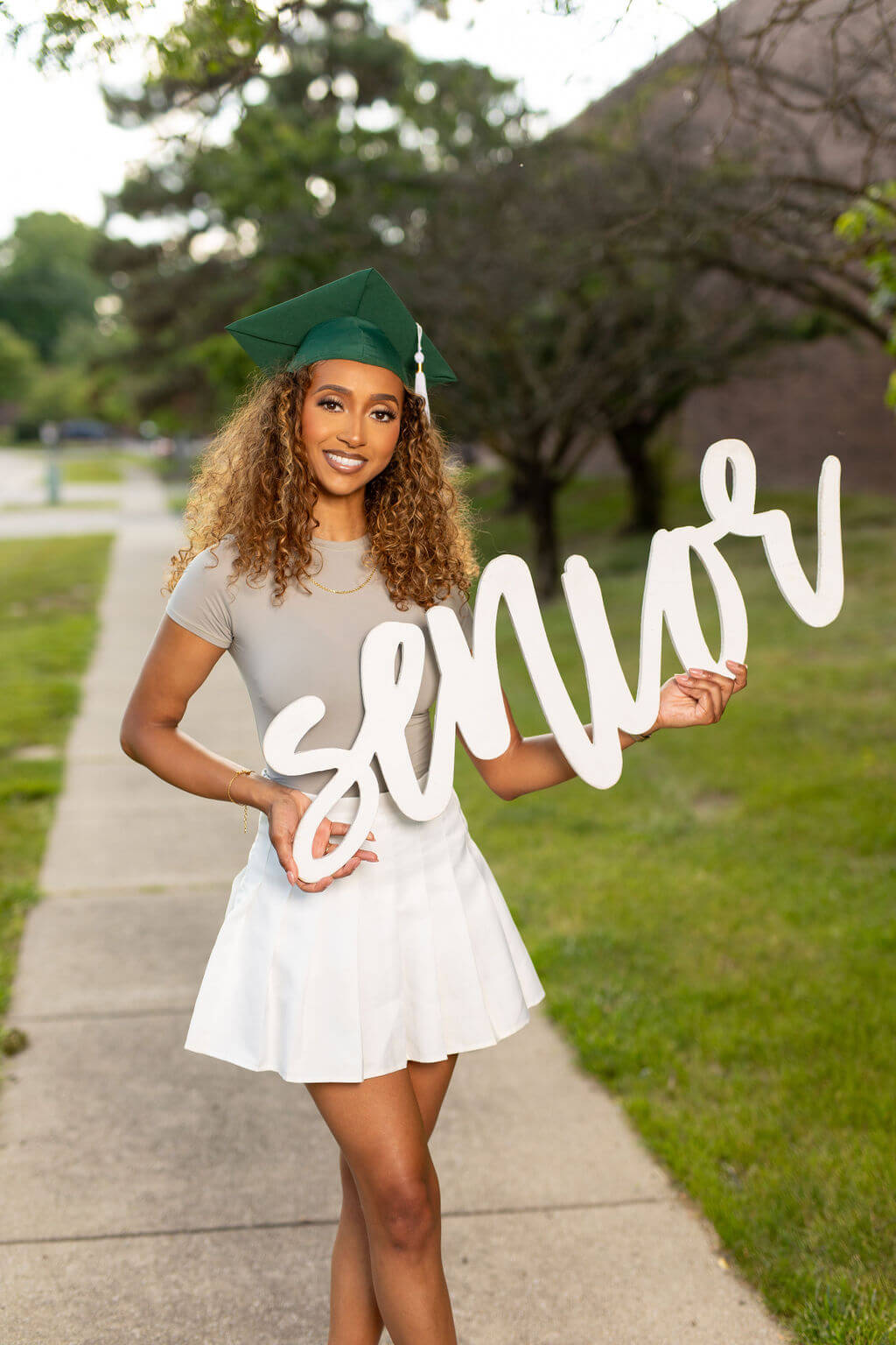 Senior Model is holding a white 36 inch photo prop that says "senior!" Standing on a Sidewalk.