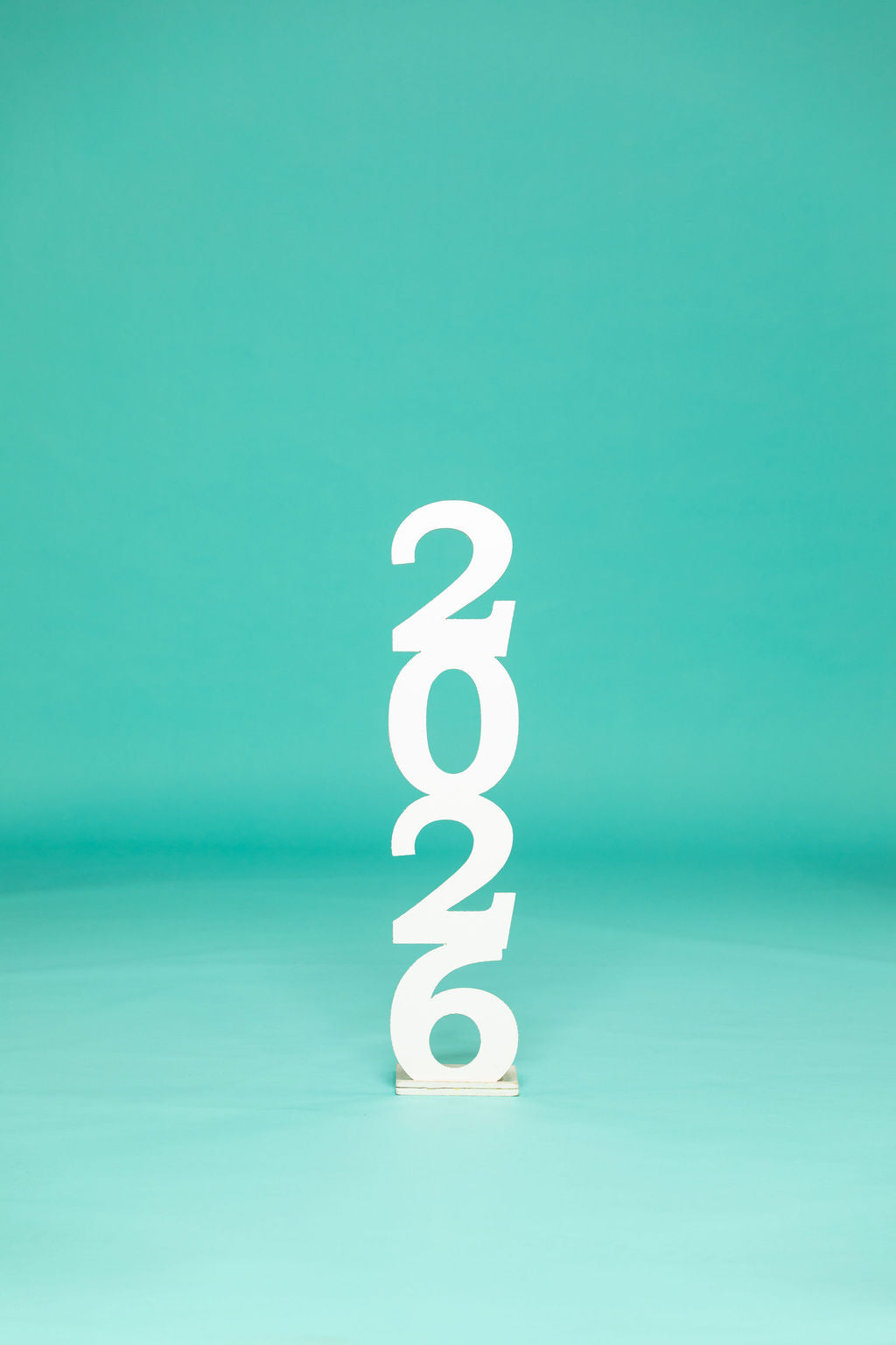 Studio display of stacked white “2026” numbers centered against a teal backdrop. 2026 senior props available now at collageandwood.com.