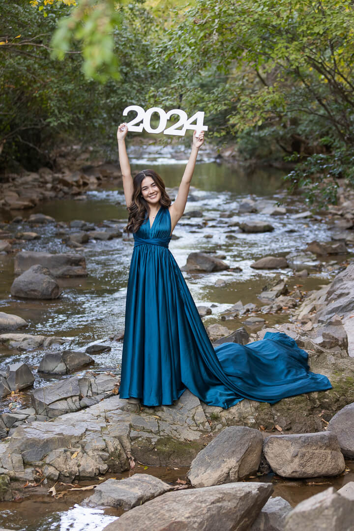 outdoor senior photo shoot with wooden white 2024. Senior is holding the sign above her head.