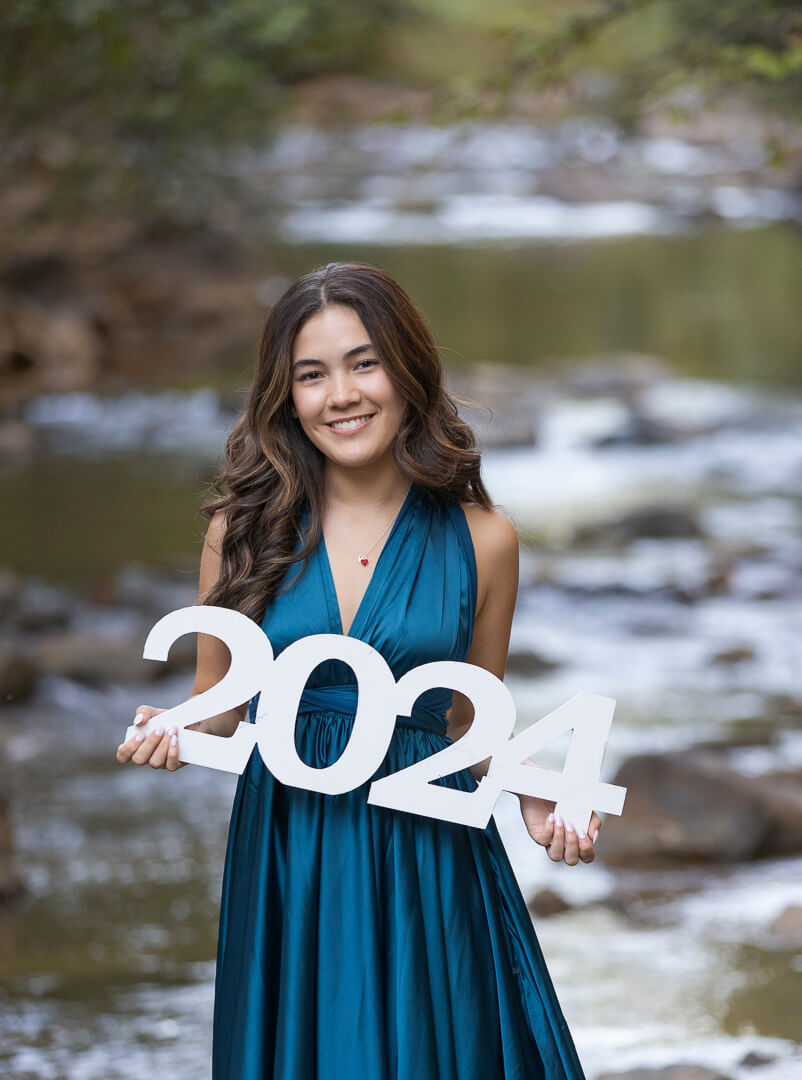 outdoor senior photo shoot with wooden white 2024 in front of creek.