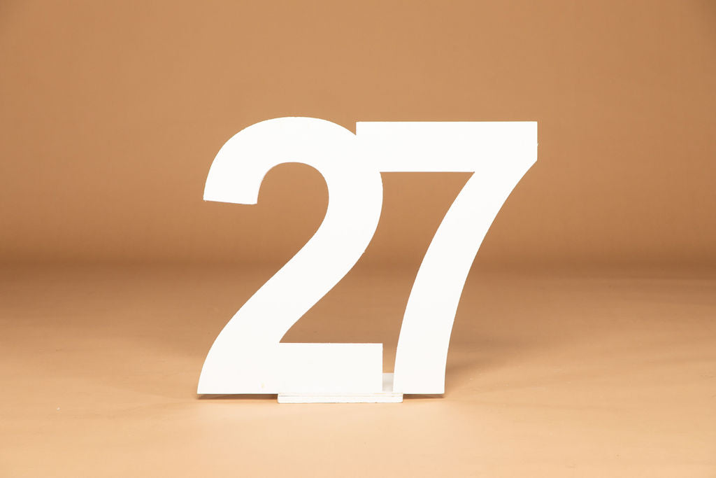 A white freestanding number 27 tabletop sign on a small handmade base, set against a warm tan studio background. Available at collageandwood.com.