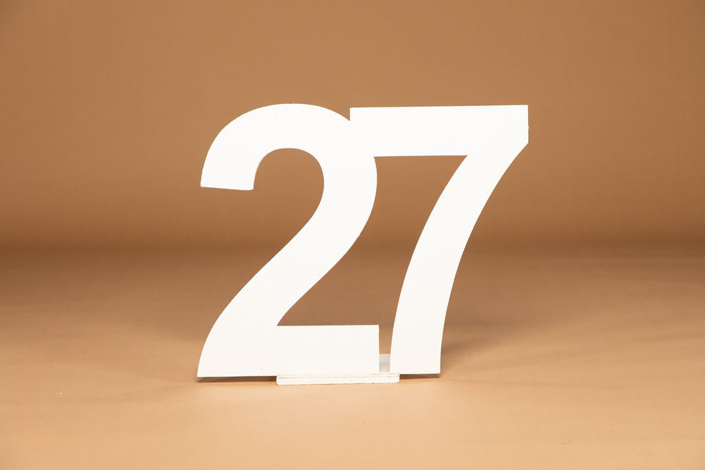 White wooden number 27 tabletop sign on a small handmade stand, set against a warm brown background. Available at collageandwood.com.