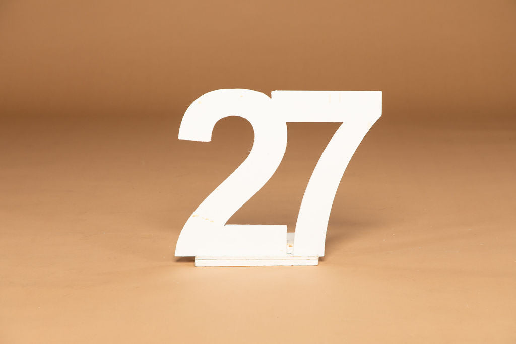 A white freestanding number 27 sign, made of wood, displayed on a warm brown background.