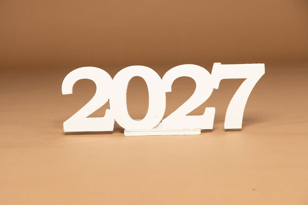 White 3D wooden numbers displaying '2027' on a matching light brown wooden surface and background.