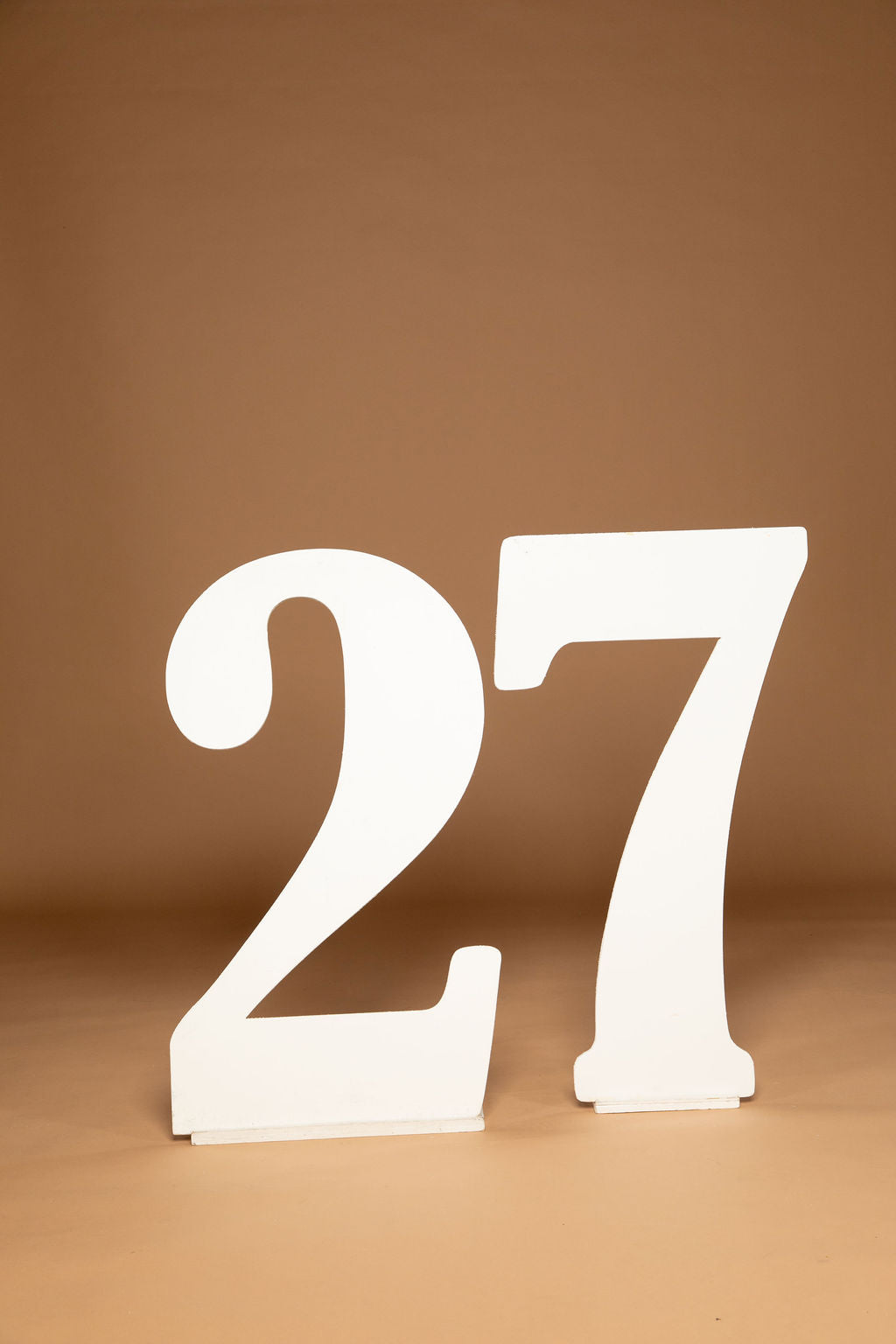 White freestanding floor number 27 sign on a warm brown studio background.
