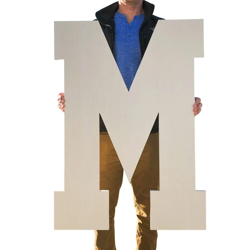Person holding a giant unfinished wooden letter M