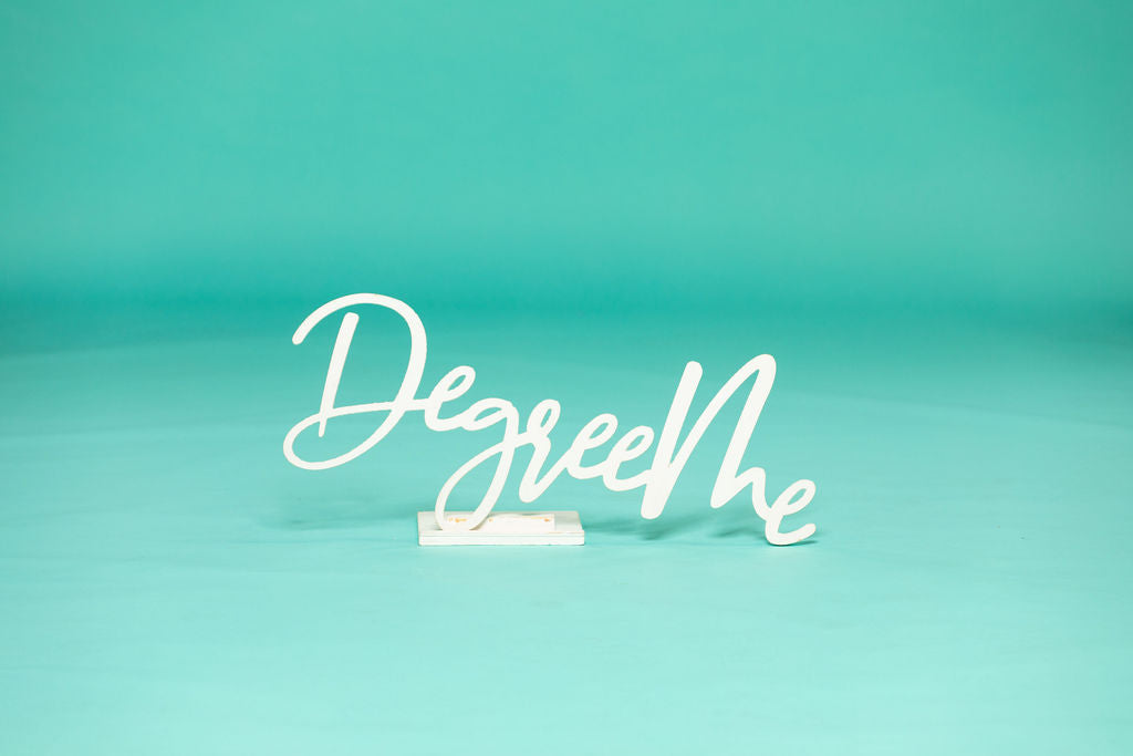 Script-style “DegreeMe” word prop displayed alone on a teal background, ideal for senior photos. Degree Me props available now at collageandwood.com.