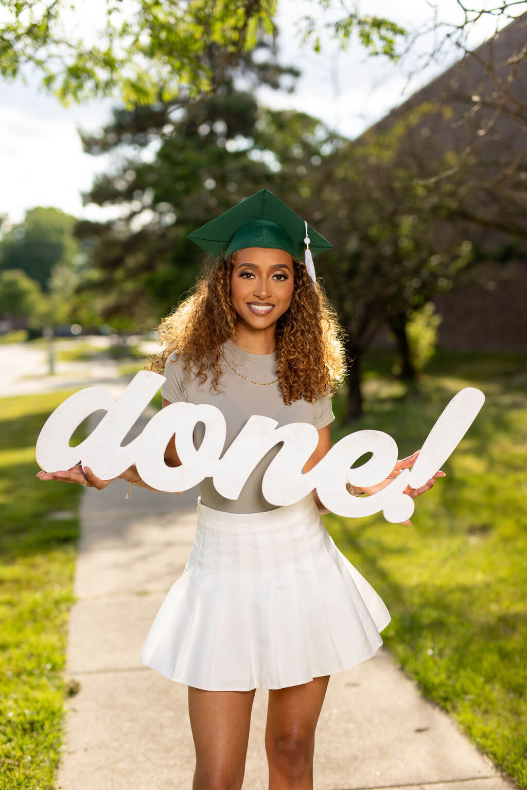 Senior model posing with "done!" photo prop. Model is outside on the sidewalk.