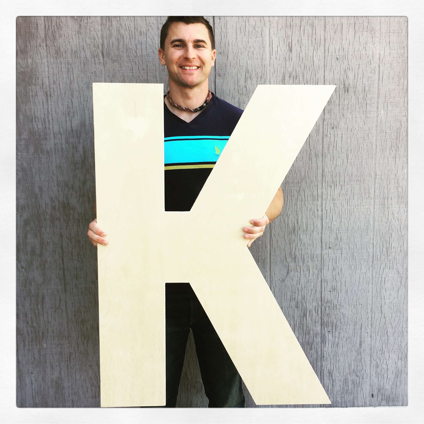 Man holding a large wooden letter K decor piece, demonstrating its impressive size and versatility as a bold statement piece for any room.