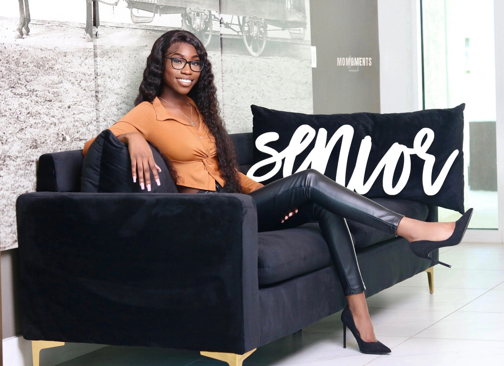 Girl sitting on a coach with "senior" photo prop.