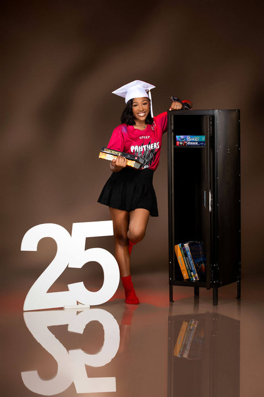 A high school senior in a red Panthers tee, black skirt, and red socks leans against an open locker filled with books, with a large "25" number sign from CollageandWood.com at her feet.