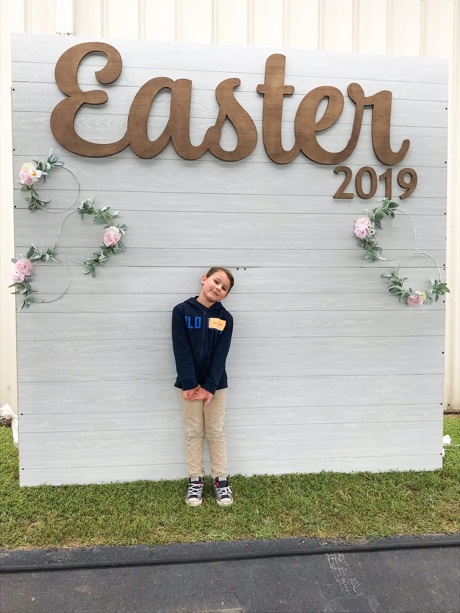 Wooden “Easter” sign hanging on a white backdrop with greenery and flowers, perfect for a church photo wall to celebrate Jesus. Ideal for window displays or Easter shop decor. Add to cart now before it becomes unavailable — checkout with ease and choose the size you prefer.